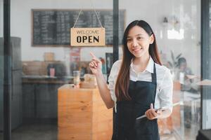 une de bonne humeur café propriétaire des stands par le 'accueillir ouvrir' signe à sa vitrine, tablette dans main, prêt à saluer les clients dans le chaud atmosphère de sa café magasin. photo