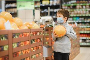 garçon porte protégé masque dans magasin. achats temps pendant coronavirus épidémie.boy dans une médical masque. quarantaine et protection virus, grippe, épidémie COVID-19 [feminine. coronavirus quarantaine photo