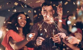 émotions sincères. des amis multiraciaux célèbrent le nouvel an et tiennent des lumières du bengale et des verres avec un verre photo