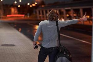 montre les pouces vers le haut. jeune homme avec sac essayant d'arrêter la voiture parce qu'il est en retard photo