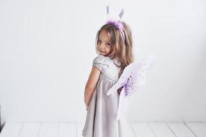 regard timide. jolie petite fille dans le costume de fée debout dans la chambre avec un fond blanc photo