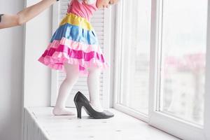 photo de jeune fille mignonne en vêtements colorés debout sur le rebord de la fenêtre