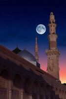 une mosquée avec le plein lune dans le ciel. masjid nabi de médina, mosquée à nuit. masjid nabi de médina. vert dôme et lune.. photo