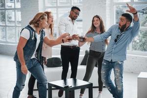 faisons un coup. les jeunes passent du bon temps au bureau. souriant et buvant avec des fenêtres en arrière-plan photo