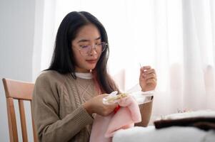 une magnifique asiatique femme est se concentrer sur couture à la main une modèle sur tissu sur un broderie Cadre. photo