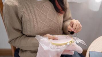 une femme est couture à la main une modèle sur un broderie cadre, profiter sa loisir à maison. photo