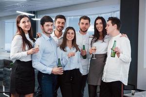 célébration du succès. photo d'une jeune équipe en vêtements classiques tenant des boissons dans le bureau moderne bien éclairé