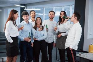 se reposer ensemble après le travail. photo d'une jeune équipe en vêtements classiques tenant des boissons dans le bureau moderne bien éclairé