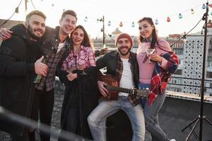 humeur géniale. fête sur le toit. cinq beaux amis qui posent pour la photo avec de l'alcool et de la guitare