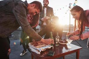 le soir arrive. que le soleil crée une atmosphère chaleureuse. manger de la pizza à la fête sur le toit. les bons amis ont un week-end avec de la nourriture délicieuse et de l'alcool photo