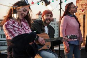 toucher l'âme. trois amis s'amusent en chantant des chansons de guitare acoustique sur le toit photo