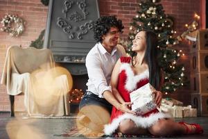 se regarder avec amour. beau couple célébrant le nouvel an dans la salle décorée avec arbre de noël et cheminée derrière photo