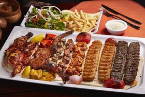 épicé un barbecue mixte grillades plat avec tikka boti des kababs, frites, salade et raita servi dans plat isolé sur table côté vue de milieu est nourriture photo