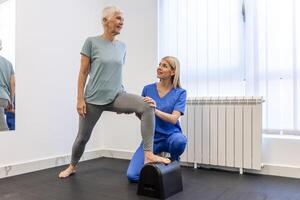 Sénior patient à le physiothérapie Faire physique des exercices avec sa thérapeute, Faire jambe physiothérapie pour personnes âgées femme, à traiter arthrose et nerf douleur dans le jambe. photo