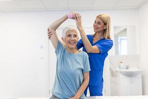 médecin ou physiothérapeute travail examiner traiter blessé bras de Sénior femelle patient, élongation et exercer, Faire le réhabilitation thérapie douleur dans clinique. photo