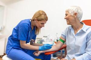 préparation pour du sang tester avec Sénior femme par femelle médecin médical uniforme sur le table dans blanc brillant chambre. infirmière perce le les patients bras veine avec aiguille Vide tube. photo