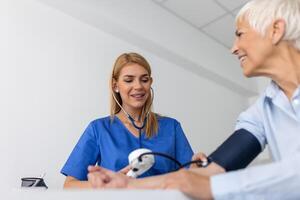 mesure du sang pression. Sénior femme avoir une visite avec femelle médecin dans moderne clinique. mesure du sang pression. pression jauge. hypertension et haute cœur taux photo