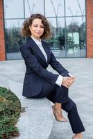 portrait de une réussi affaires femme dans de face de moderne affaires bâtiment. Jeune directeur pose dehors. femelle affaires chef photo