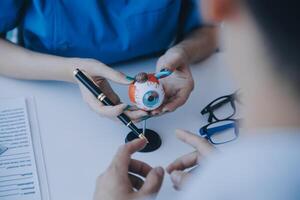 fermer de asiatique femelle médecin parlant avec personnes âgées patient montrant globe oculaire modèle et expliquant œil maladie dans hôpital photo