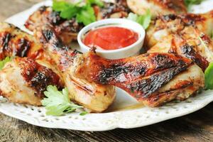 grillé poulet jambes sur en bois table servi sur blanc assiette avec coriandre photo