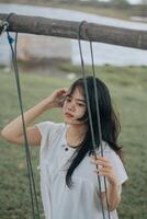 une enfance rêver de en volant haute sur une balançoire dans une parc. une Jeune fille dans une blanc robe monte sur une balançoire photo