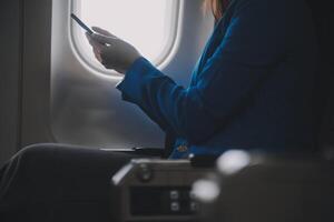 en utilisant mobile et ordinateur portable, réfléchi asiatique gens femelle la personne à bord, avion fenêtre, à la perfection Capturer le anticipation et excitation de vacances Voyage. Chinois, Japonais personnes. photo