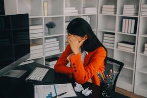 femmes asiatiques assises dans un bureau à domicile avec stress et fatigue oculaire. femme d'affaires fatiguée tenant des lunettes et massant le pont du nez. il y a des tablettes, des ordinateurs portables et du café. photo