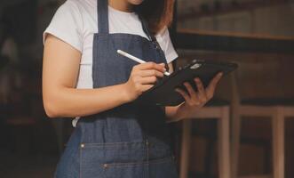 startup réussie propriétaire de petite entreprise PME beauté fille stand avec tablette smartphone dans un café-restaurant. portrait d'une femme asiatique bronzée propriétaire d'un café barista. PME entrepreneur vendeur concept d'entreprise photo