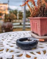 cigarette brûlant avec fumée sur céramique cendrier et sec plante décoration photo