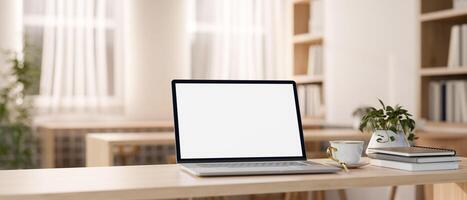 une Écran blanc portable ordinateur sur une en bois table dans une magnifique minimaliste bibliothèque ou librairie. photo