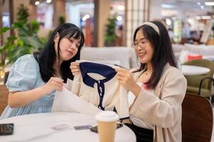 deux Jeune asiatique femmes asseoir dans une café à une achats centre commercial, examiner vêtements ils ont acheté. photo