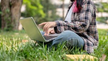une tondu image de une femelle en utilisant sa portable ordinateur tandis que séance sur le herbe dans une parc. photo