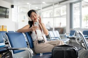 une détendu femelle touristique passager est profiter le la musique sur sa écouteurs dans le aéroport Terminal. photo