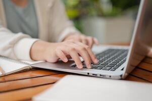 une tondu image de une femme est travail à distance à un Extérieur espace, dactylographie sur portable clavier. photo