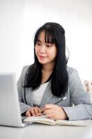 une Jeune asiatique femme d'affaires est à la recherche à sa portable écran tandis que prise Remarques dans le carnet. photo