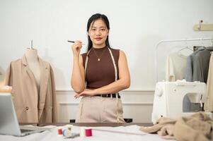 un attrayant asiatique femelle mode designer ou tailleur est dans sa studio, souriant à le caméra. photo