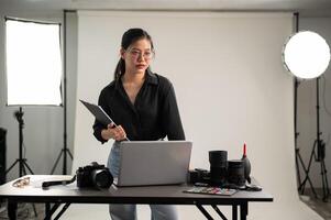 un élégant asiatique femelle photographe dans une noir chemise est permanent dans sa séance photo studio.