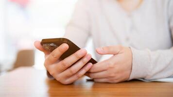 une tondu coup de un asiatique femme en utilisant sa téléphone intelligent à une table dans une confortable café magasin. photo