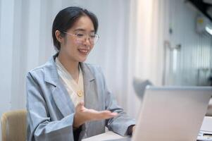 une sur de soi asiatique femme d'affaires est ayant un en ligne réunion avec sa client, travail dans sa bureau. photo