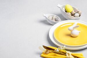 Pâques table portion. blanc Jaune vaisselle, Caille œufs, d'or coutellerie, blanc céramique lapin sur gris photo