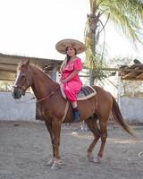 mexicain femme portant traditionnel robe et charro chapeau sur à cheval. cinco de mayo fête. photo