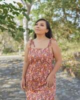 femme portant robe avec fleurs admiratif la nature dans une Publique parc. ensoleillé été journée. photo