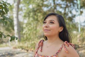 femme portant robe avec fleurs admiratif la nature dans une Publique parc. ensoleillé été journée. photo