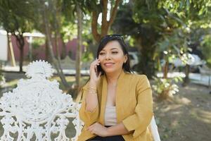 femme assise sur une parc banc parlant sur le téléphone. ensoleillé journée. photo