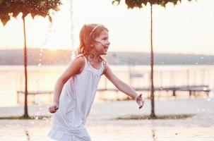 souriant et heureux. jeune fille joue dans la fontaine à la chaleur estivale et au fond du lac et des bois photo