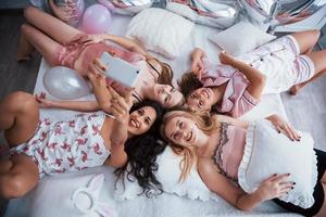 aime se rencontrer. prendre un selfie avec des amis en position allongée sur le lit à l'enterrement de vie de jeune fille photo