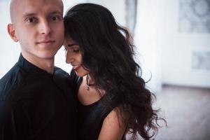 portrait de couple heureux à l'intérieur. un homme chauve et une femme brune se tiennent dans la salle blanche photo