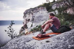 seul homme assis près d'un feu de camp, essayant de maintenir le feu au bord de la montagne photo