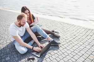 deux étudiants gars et fille sont assis à l'extérieur et profitent d'un ordinateur portable, étudient à l'extérieur par une journée ensoleillée photo