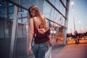 une belle jeune fille avec un sac à dos derrière ses épaules, debout dans la rue près d'un aéroport. elle vient d'arriver du reste et très contente